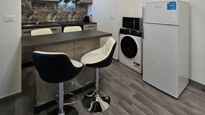 Ett kompakt kök med tvättmaskin, kylskåp och två barstolar.