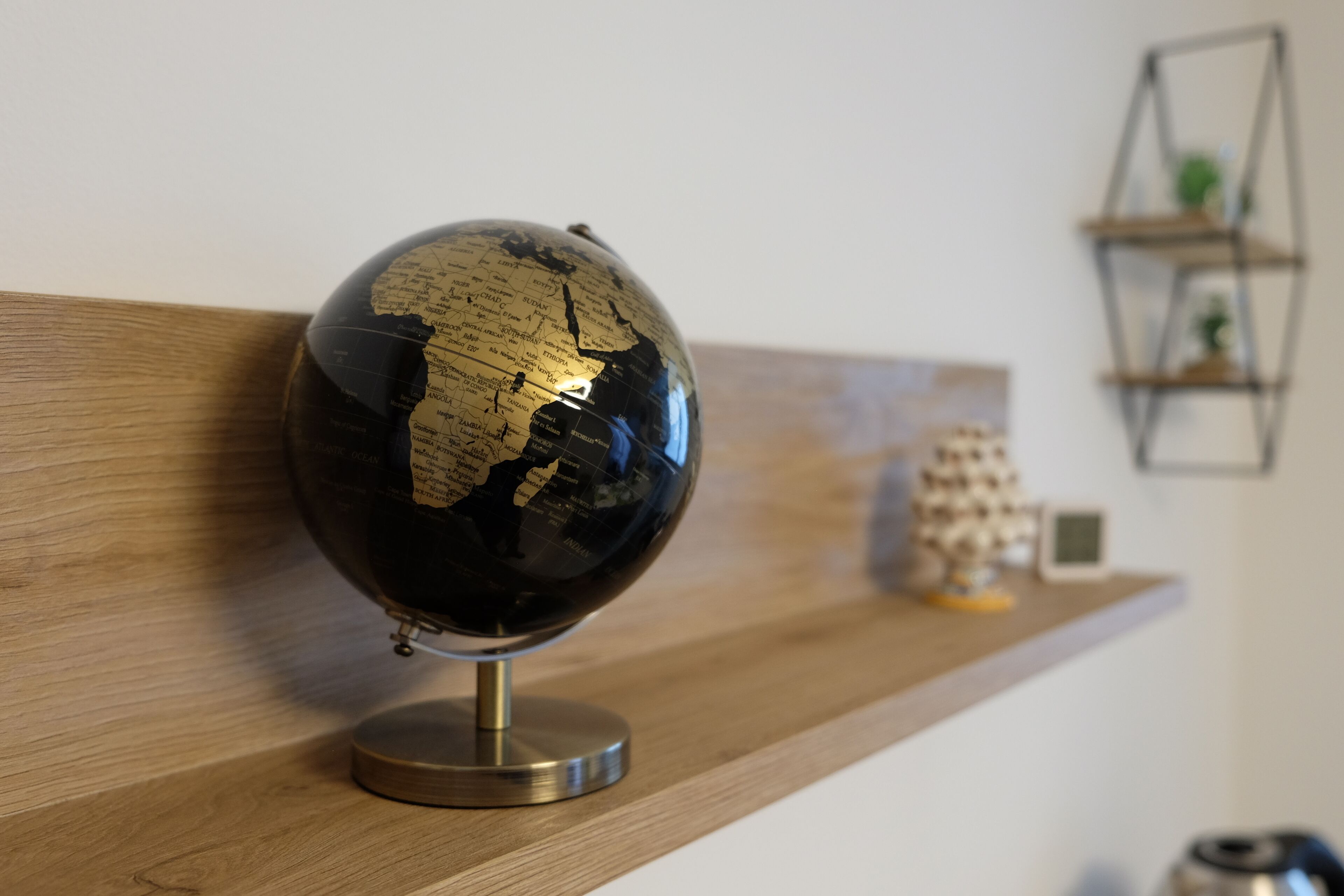 Un globe terrestre posé sur une étagère en bois, soutenu par un pied en métal.
