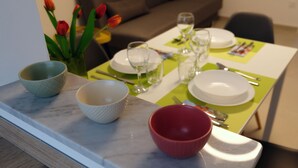 Et spisebord dækket med tallerkener, skåle og bestik, med en vase med tulipaner ved siden af.