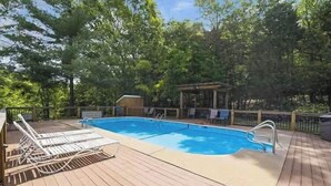 Ett trädäck med en pool, solstolar och en lusthus.