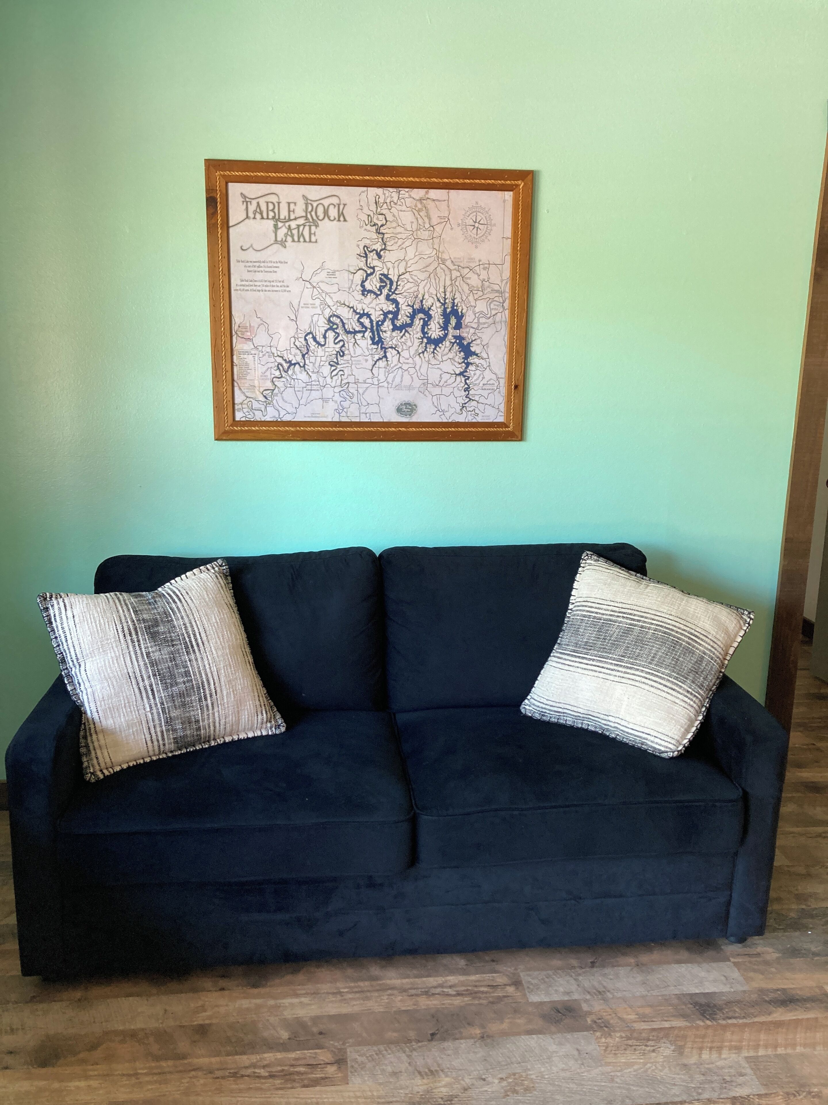 Un canapé bleu foncé agrémenté de deux coussins à rayures, placé devant un mur vert clair. Au-dessus du canapé, on peut voir une carte encadrée du lac Table Rock.