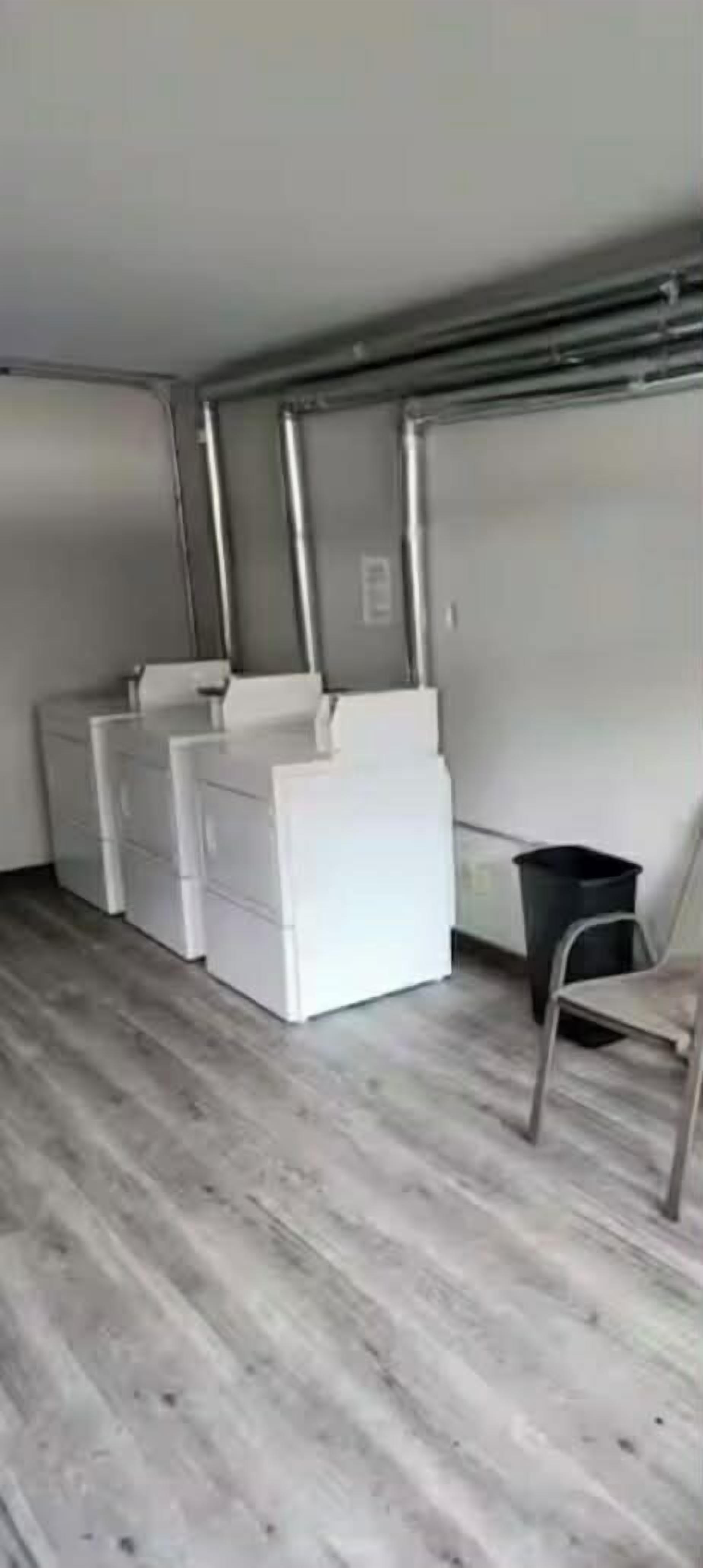 Huoneessa on puulattia, valkoinen lipasto, musta roskakori ja metallinen tuoli.