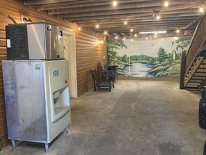 A basement with a refrigerator, a water dispenser, a mural of a forest, a table with chairs, and a staircase.