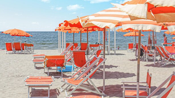 Una playa con hileras de sombrillas anaranjadas y blancas y sillones de baño naranja.