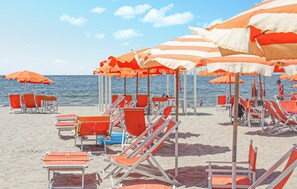 A beach with rows of orange and white striped umbrellas and orange lounge chairs. - Nice home in Azzano with WiFi (Azzano)