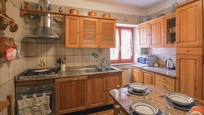 Una cocina con armarios de madera, encimera de granito, pileta de acero inoxidable, estufa y ventana con cortinas.