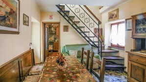 Un área de comedor con mantel floreado, una escalera con barandilla decorativa y una cocina al fondo.