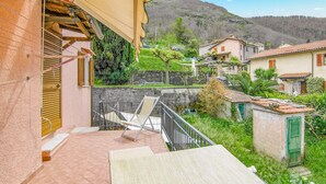 Un balcón con una silla, una mesita y vistas a una colina con casas.