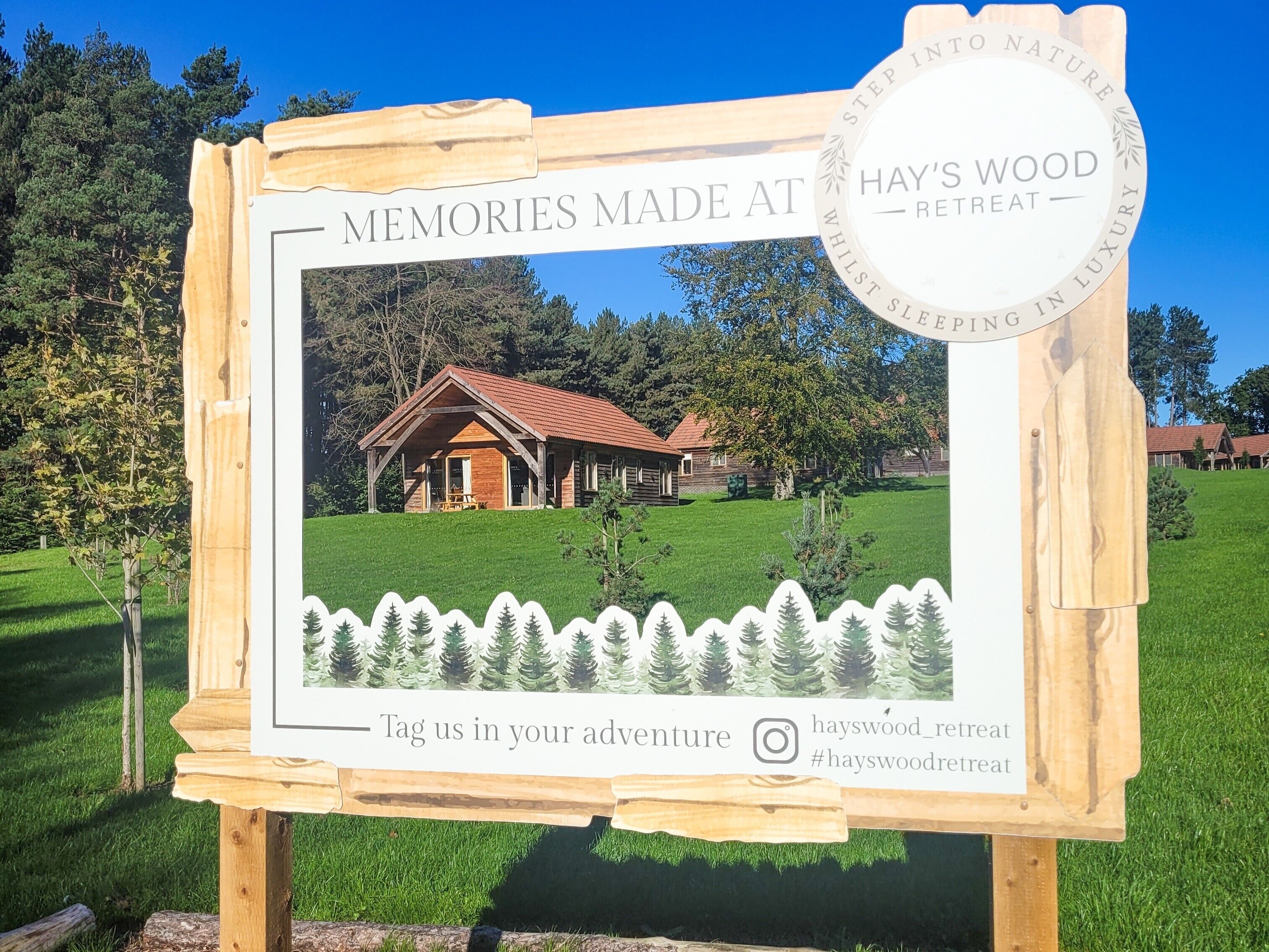 A wooden sign with a photograph of a lodge, a logo, and a hashtag for social media.