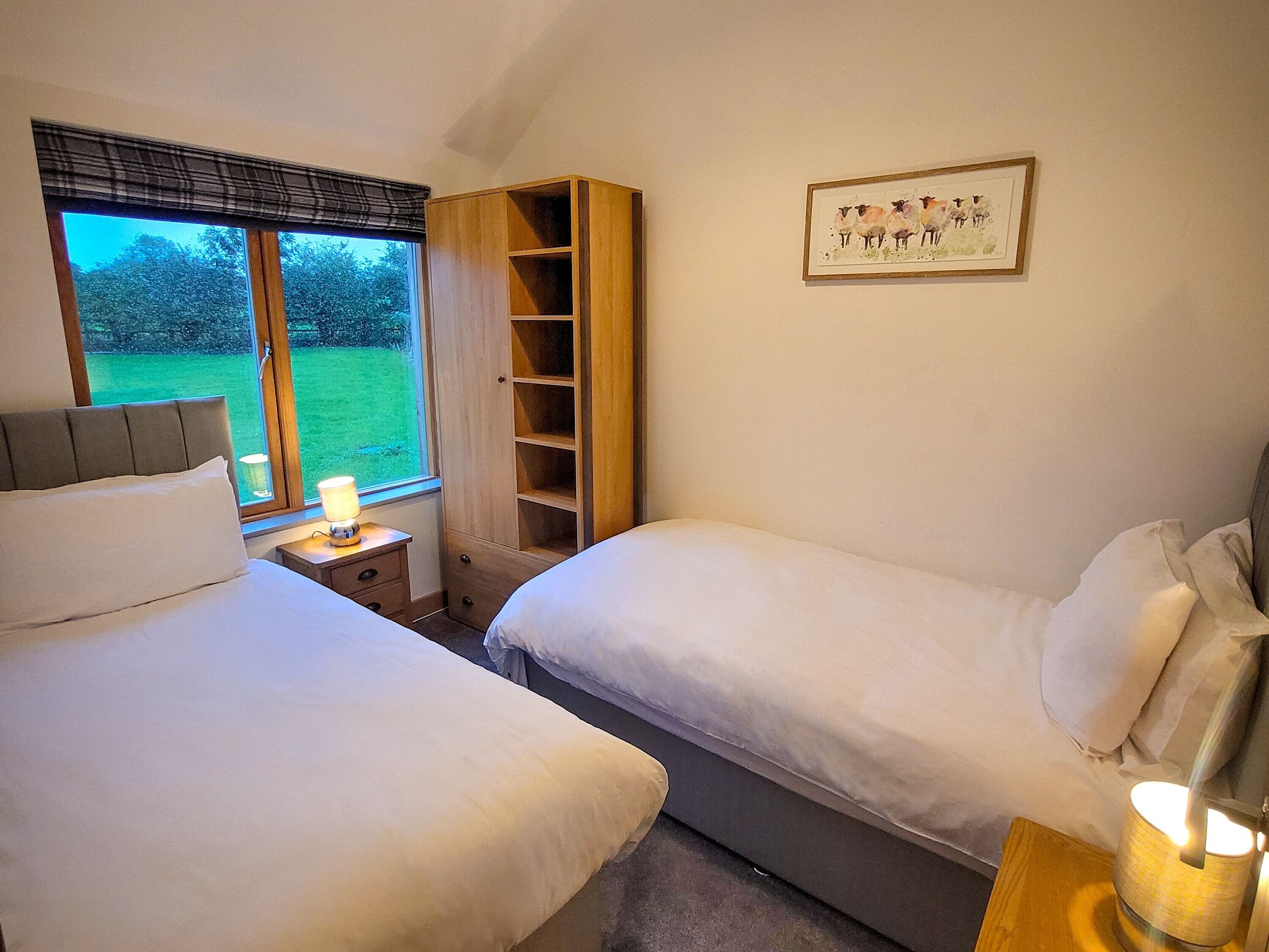 A bedroom with two beds, a bedside table with a lamp, a wardrobe, and a framed picture on the wall.