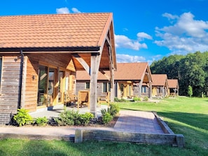 A row of wooden cabins with pitched roofs, each featuring a porch and a window. - Hay's Wood Retreat (King's Lynn)