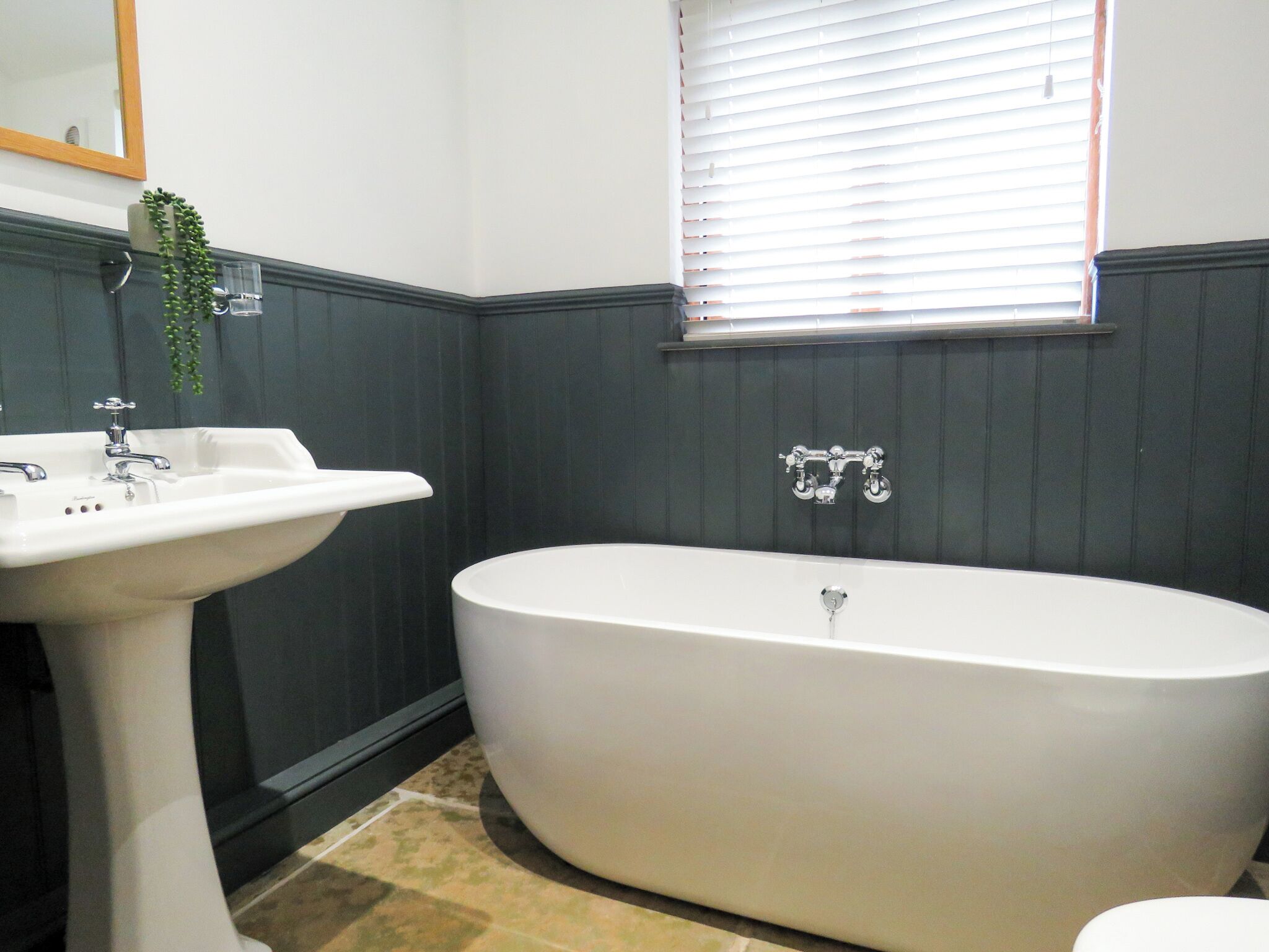 A bathroom with a freestanding bathtub, a pedestal sink, a mirror, and a window with blinds.