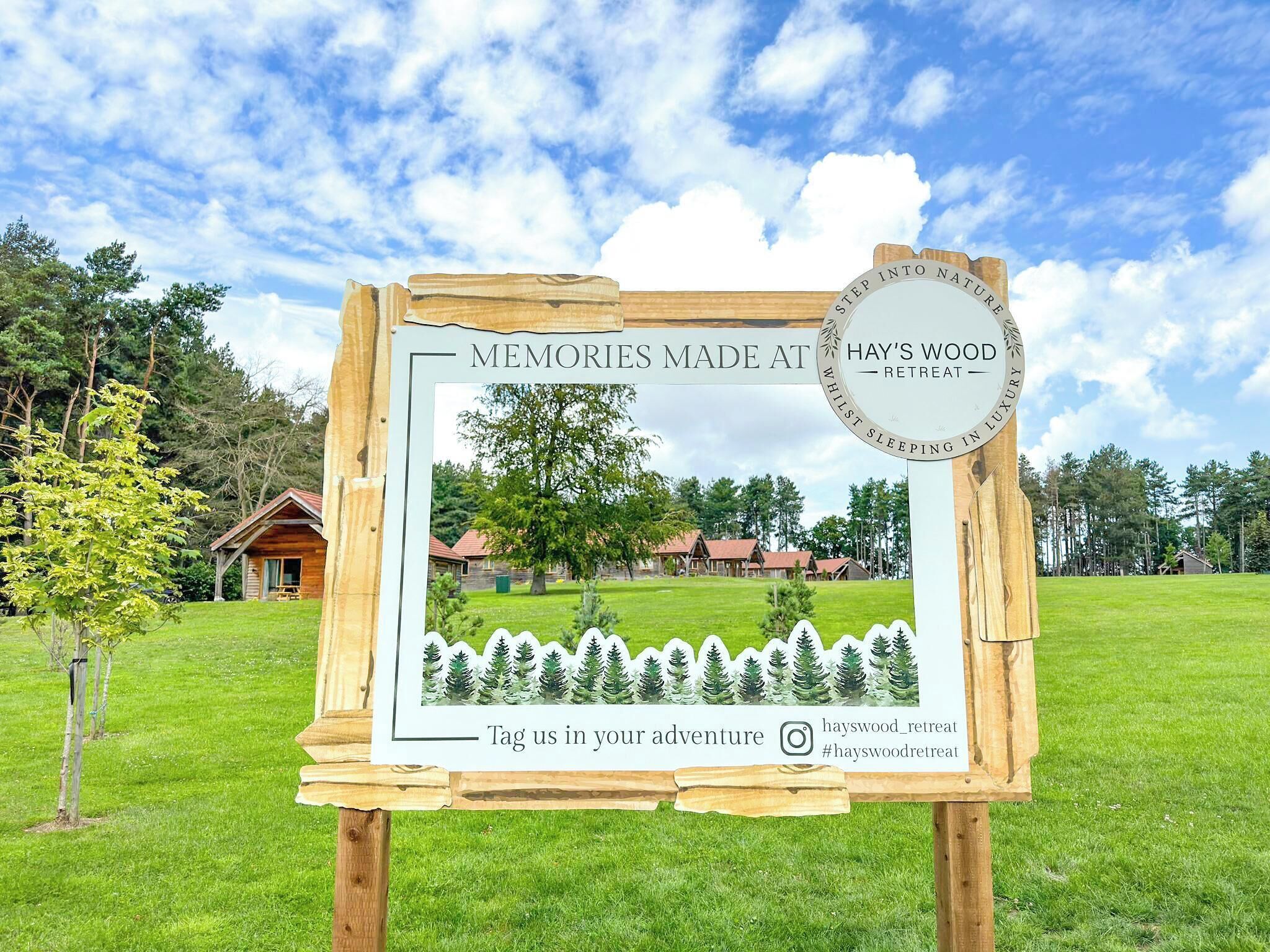Placa de madeira com imagem de um retiro, um logotipo e texto convidando visitantes a participar da aventura.