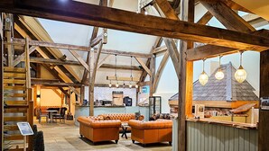 A rustic interior with exposed wooden beams, a lofted seating area with leather sofas, and a bar counter. - Hay's Wood Retreat (King's Lynn)