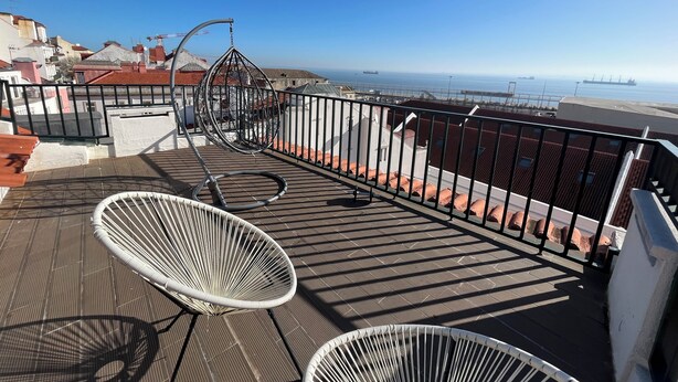 A rooftop terrace with two white wicker chairs, a metal swing, and a view of the sea and ships. - New House, Amazing View (Lisboa)