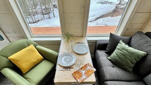 Ein gemütliches Wohnzimmer mit einem grünen Sessel, einem grauen Sofa und einem Holztisch, gedeckt für zwei Personen.