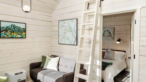 A cozy room with a loft bed, a ladder, a sofa, and a painting on the wall.