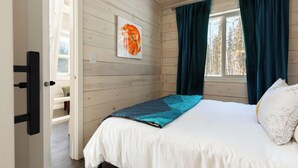 Een slaapkamer met een bed, een raam met gordijnen, een houten wand en een deur.