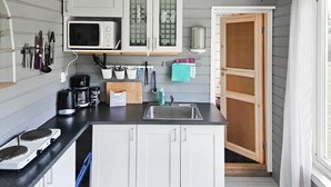 Een kleine keuken met witte kastjes, een magnetron, een koffiezetapparaat en een spoelbak.