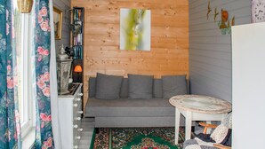 Een gezellige kamer met een houten wand, een grijze bank, een klein rond tafeltje en een kleurrijk vloerkleed.