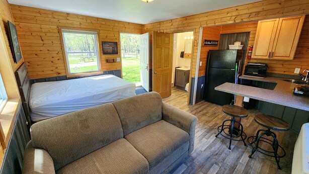 A compact room with a bed, a sofa, a small kitchen area, and a view of the outdoors.