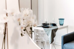 A dining area with a table set for two, clear glass stools, and a vase of white flowers.