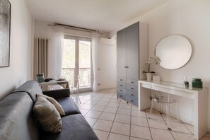 A modern room with a grey sofa, a white desk with a mirror, and a large wardrobe.