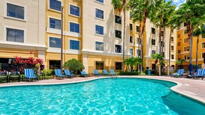 A hotel with a swimming pool surrounded by lounge chairs and palm trees.