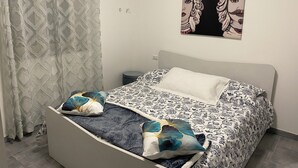 Un dormitorio con cama, ropa de cama estampada, una cortina y una obra de arte colgada en la pared.