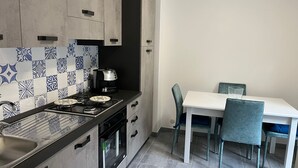Una cocina moderna con estufa a gas, horno y cafetera. Hay una mesa de comedor con sillas y un salpicadero de azulejos.