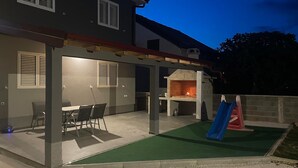 An outdoor patio with a barbecue area, a dining table with chairs, and a children's slide. - Nice home in Privlaka (Privlaka)