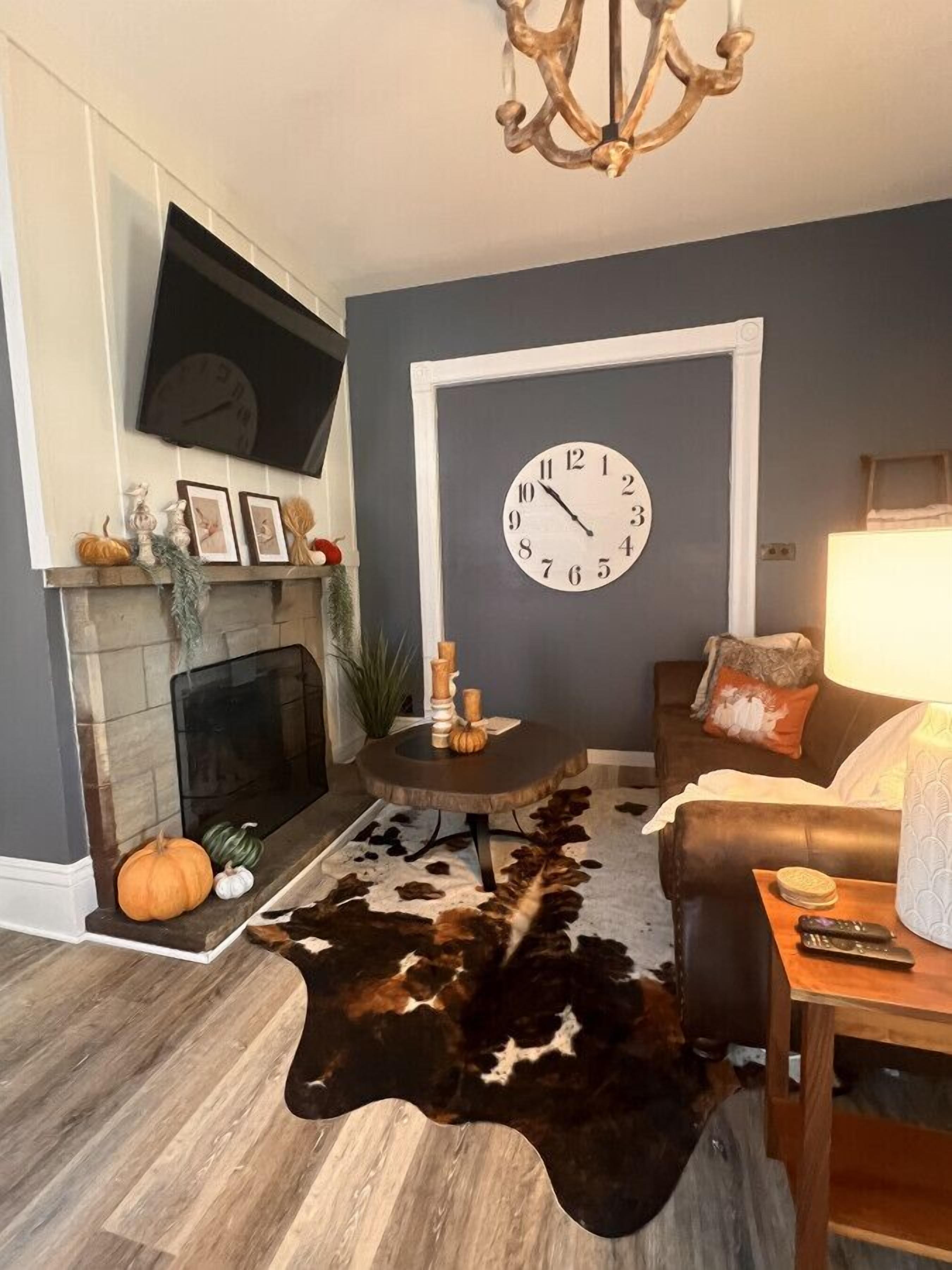 A living room with a fireplace, a large clock, a sofa, and a cowhide rug.