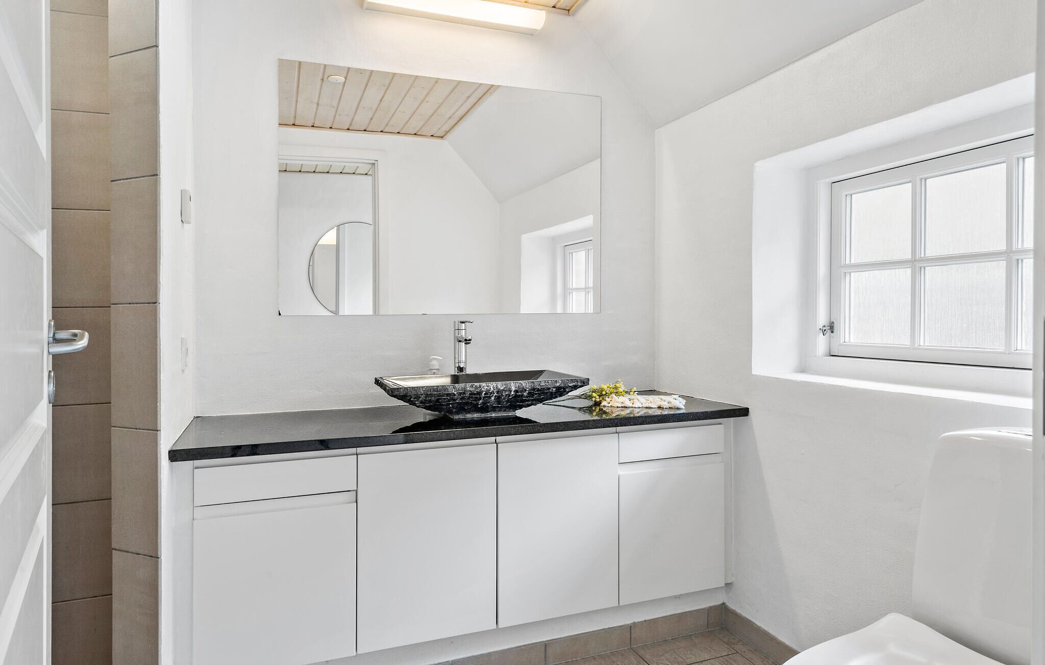 Une salle de bain moderne avec un lavabo noir, des meubles blancs et un grand miroir.