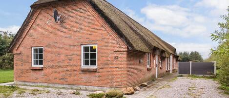 A brick building with a thatched roof, numbered 23, featuring two windows and a door.