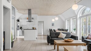A modern kitchen with white cabinets, a central island, and a dining area with a long table and chairs. - 7 bedroom lovely home in Ulfborg (Ulfborg)