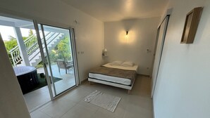 A bedroom with a bed, a sliding glass door leading to a balcony, and a small table with a chair. - Noola t4 au Robert Vive L'aventure en Famille et Entre Amis (Le Robert)