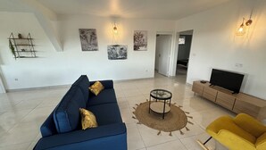 A modern living room with a blue sofa, a yellow chair, a TV on a wooden stand, and artwork on the walls. - Noola t4 au Robert Vive L'aventure en Famille et Entre Amis (Le Robert)