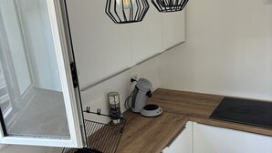 A modern kitchen with a built-in dishwasher, a sink, a coffee maker, and pendant lights with exposed bulbs. - Noola t4 au Robert Vive L'aventure en Famille et Entre Amis (Le Robert)