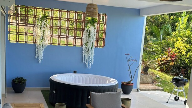 A patio area with a round table, two chairs, a sofa, and a hanging light fixture. - Noola t4 au Robert Vive L'aventure en Famille et Entre Amis (Le Robert)