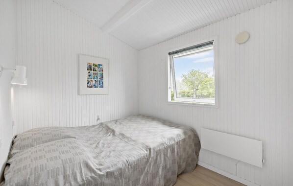 Un dormitorio con cama, ventana con vistas a árboles, radiador blanco y una foto enmarcada en la pared.
