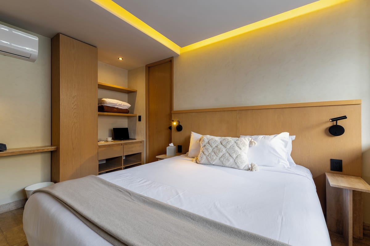 Une chambre d’hôtel moderne avec un grand lit, une tête de lit en bois, des étagères intégrées, des tables de chevet et une lampe fixée au mur.