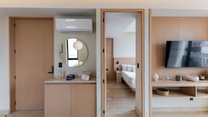 Una habitación de hotel moderna con un armario de madera, una mesita de noche, un espejo, un televisor de pantalla plana y una cama.