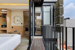 Moderni hotellihuone, jossa on sänky, pieni työpöytä, peili ja parveke, jossa on kaide.