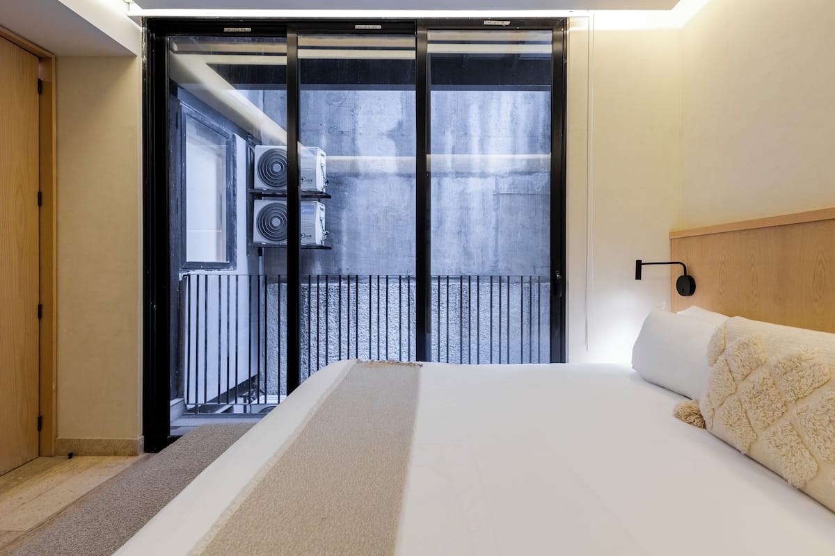 Une chambre à coucher avec un lit, une tête de lit, une fenêtre et une vue sur l’extérieur.