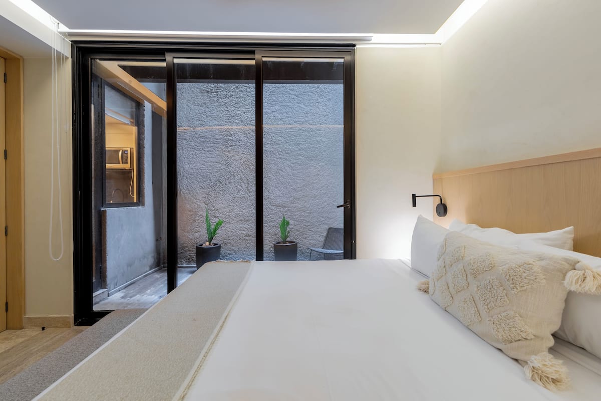 Une chambre avec un lit, une porte-fenêtre coulissante donnant sur un espace extérieur et une petite table avec des chaises.