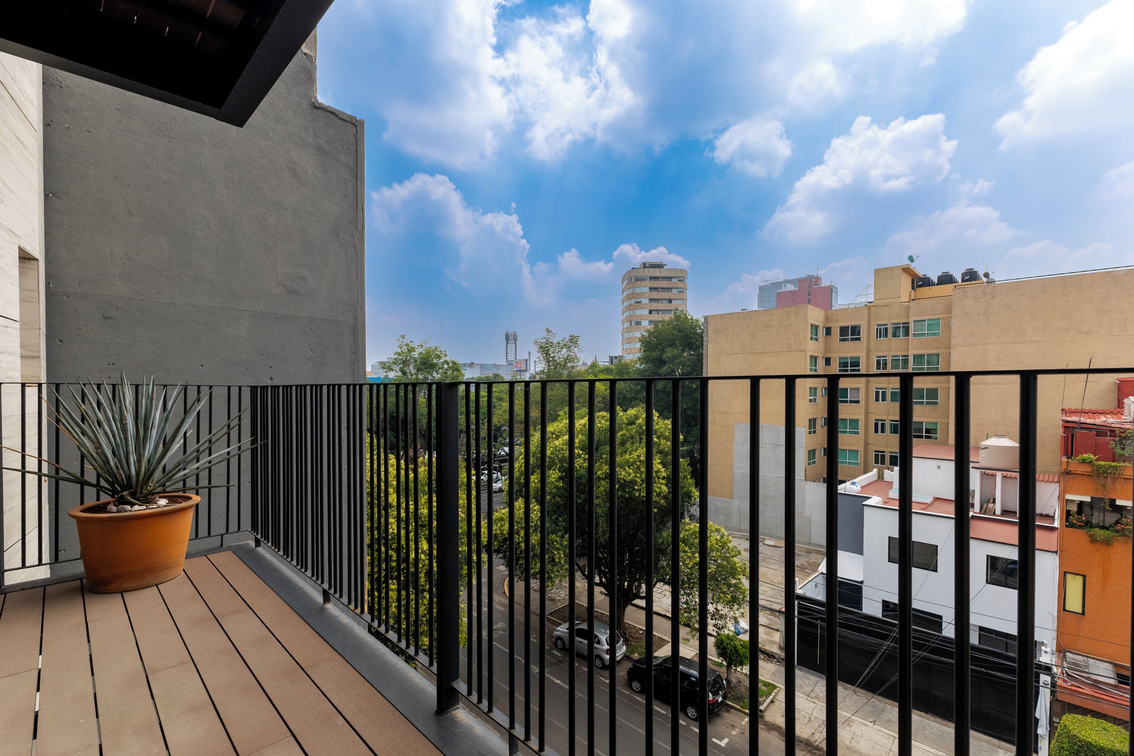 A balcony with a potted plant, a view of the street, and buildings in the background.