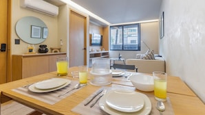 Un comedor con una mesa preparada para dos personas, un televisor y una ventana con vista a edificios.