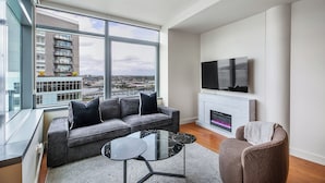 A modern living room with a grey sofa, a glass coffee table, and a fireplace. - Luxury high rise condo with river and mountain views, walk to OHSU (Portland)