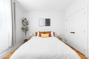 A bedroom with a large bed, two bedside tables, a nightstand, a potted plant, and two framed pictures on the wall. - 3 LEVEL LUX Townhome! Near MetLife NYC EWR PATH, 4Bed/3Bath! (Jersey City)