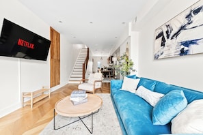 A modern living room with a blue sofa, a coffee table, and a flat-screen TV displaying 'NETFLIX'. - 3 LEVEL LUX Townhome! Near MetLife NYC EWR PATH, 4Bed/3Bath! (Jersey City)